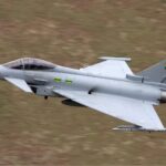 Typhoon EF 2000 military jet flies at low altitude over a blurred landscape, showcasing the Turkish Air Force modernization efforts. The aircraft, part of Turkey's Eurofighter Typhoon acquisition, boasts a delta wing design and visible emblems on the tail fin.