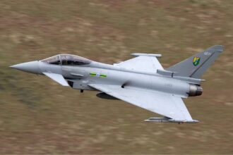 Typhoon EF 2000 military jet flies at low altitude over a blurred landscape, showcasing the Turkish Air Force modernization efforts. The aircraft, part of Turkey's Eurofighter Typhoon acquisition, boasts a delta wing design and visible emblems on the tail fin.